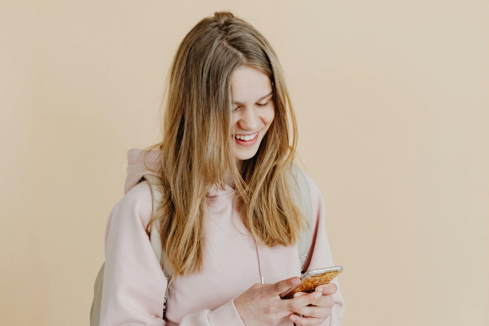 A smiling girl with a school backpack looking at her phone