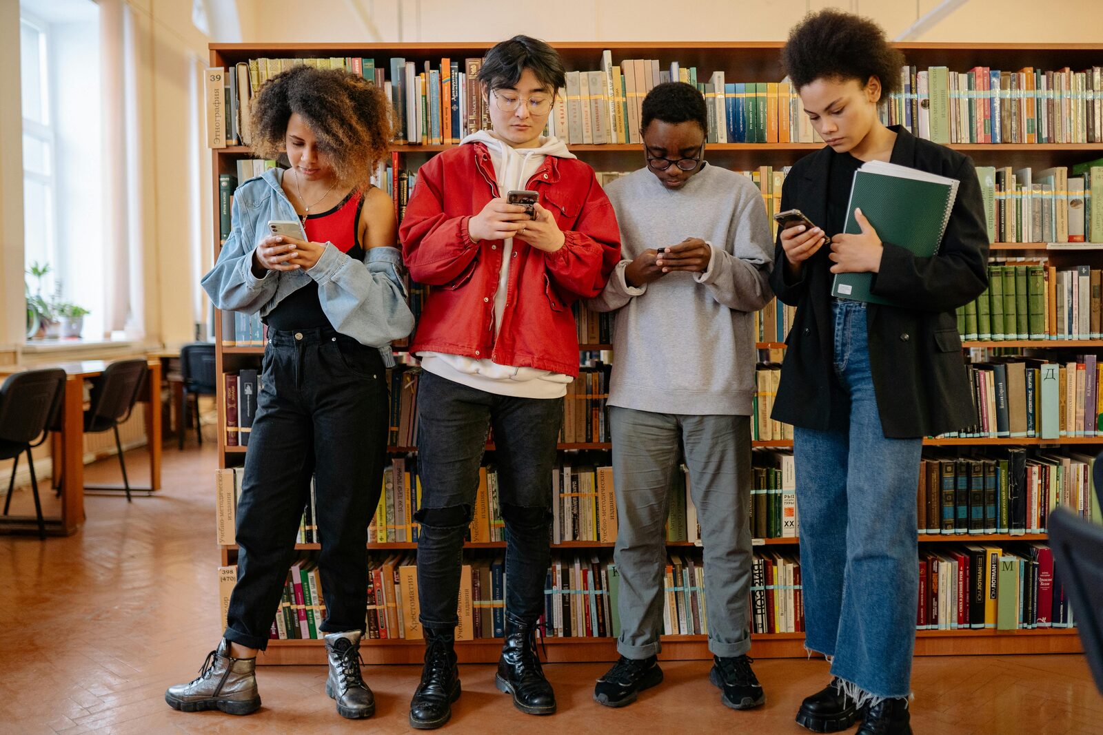 Four teenagers standing together, each absorbed in their own phone