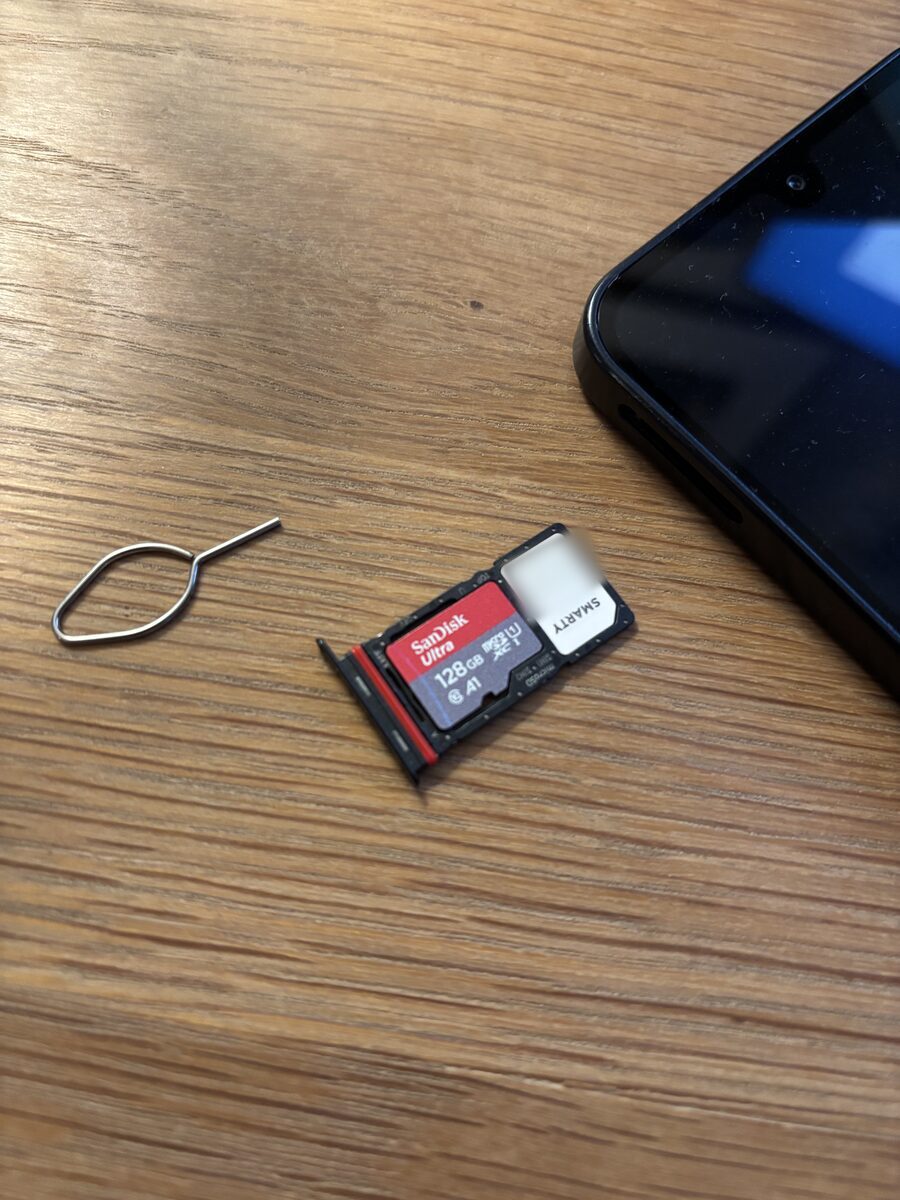 The SIM tray out of the phone, with a nano-SIM in the small slot and a microSD card in the larger one, next to the metal SIM tool